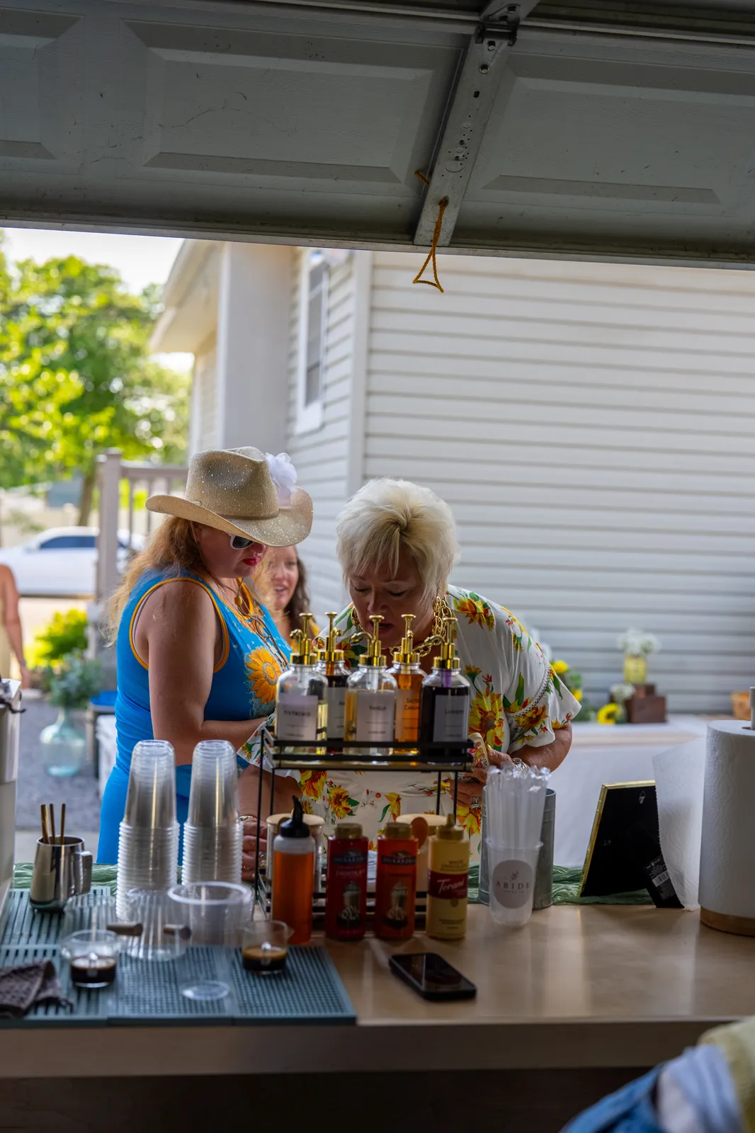The Abide Coffee Co. mobile cart set up under an open garage door, sunflowers on the counter, two guests approaching.