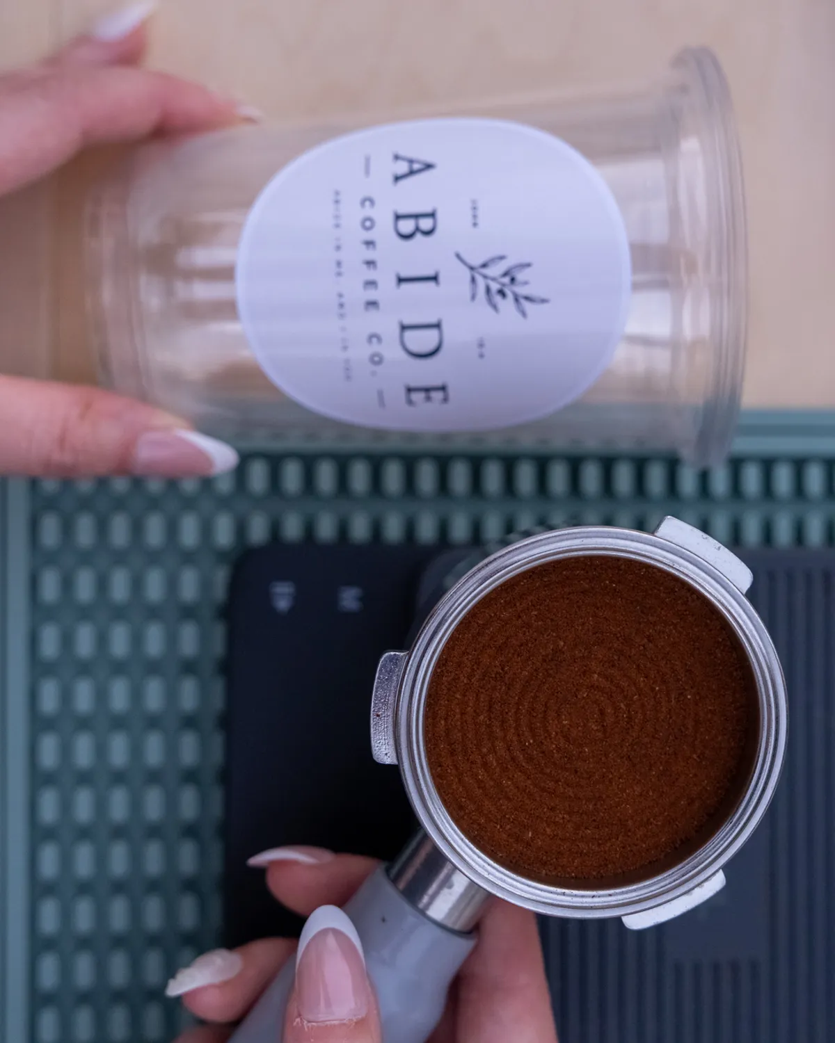 A branded Abide Coffee Co. cup and freshly tamped portafilter rest on a sage-green bar mat.