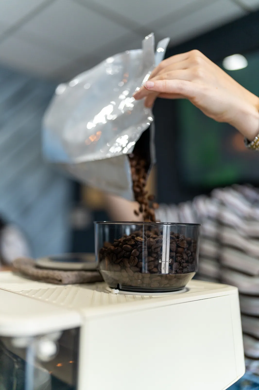 Fresh coffee beans pour from a bag into the grinder hopper.