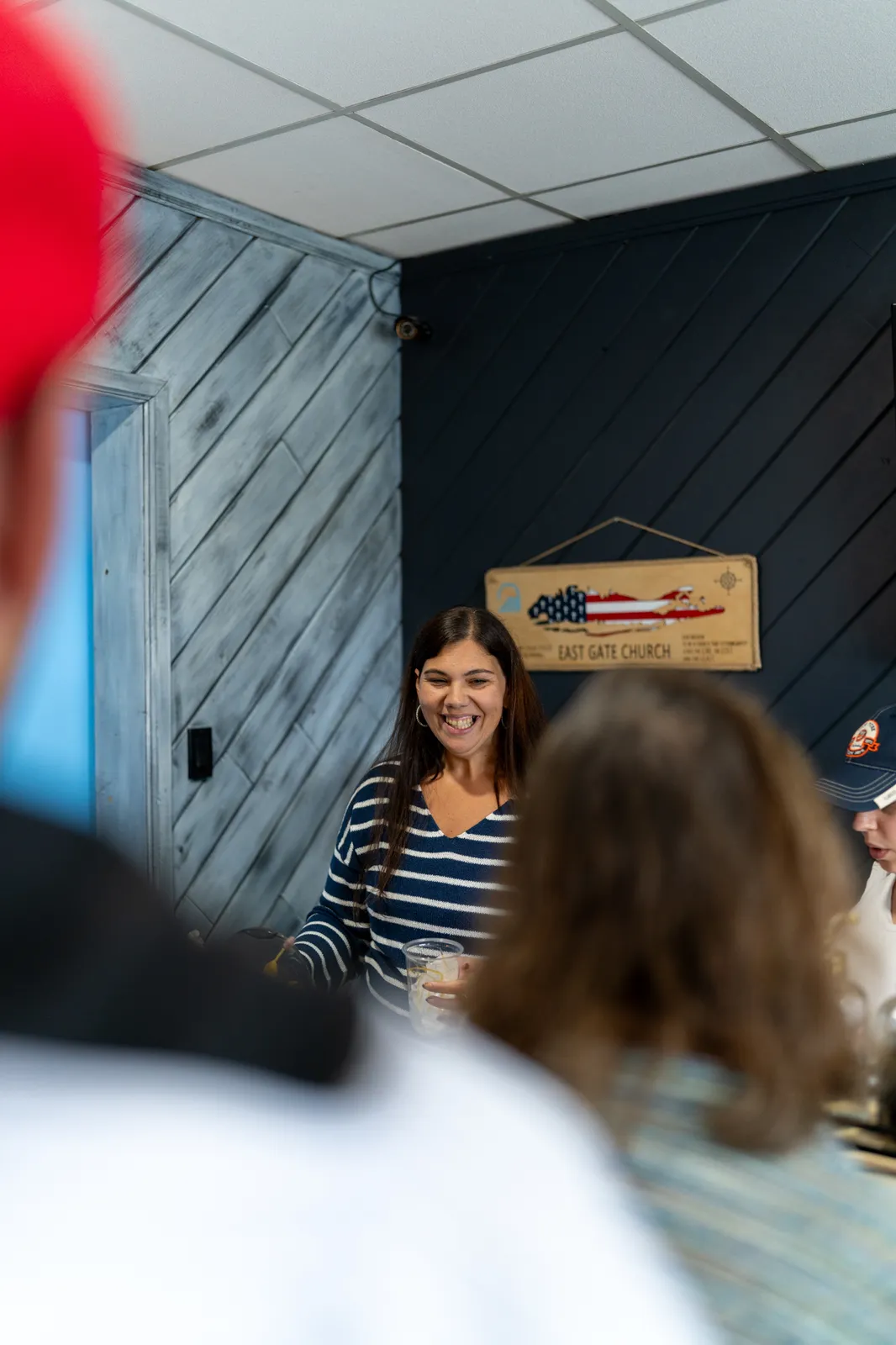 A smiling barista in a striped shirt works the bar, framed by guests in the foreground.