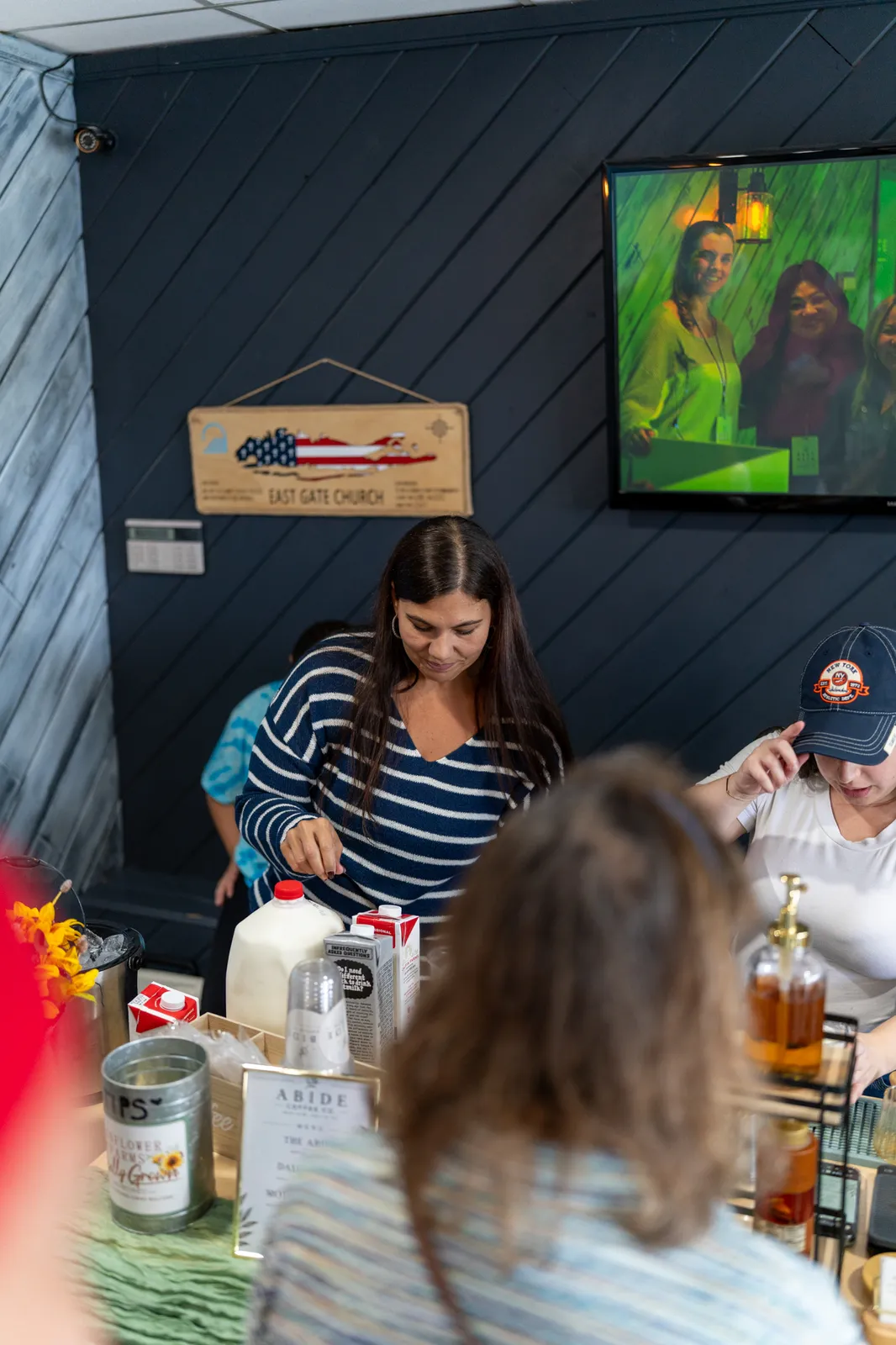 A barista in a striped shirt mixes drinks beneath the American-flag sign and lobby screen.