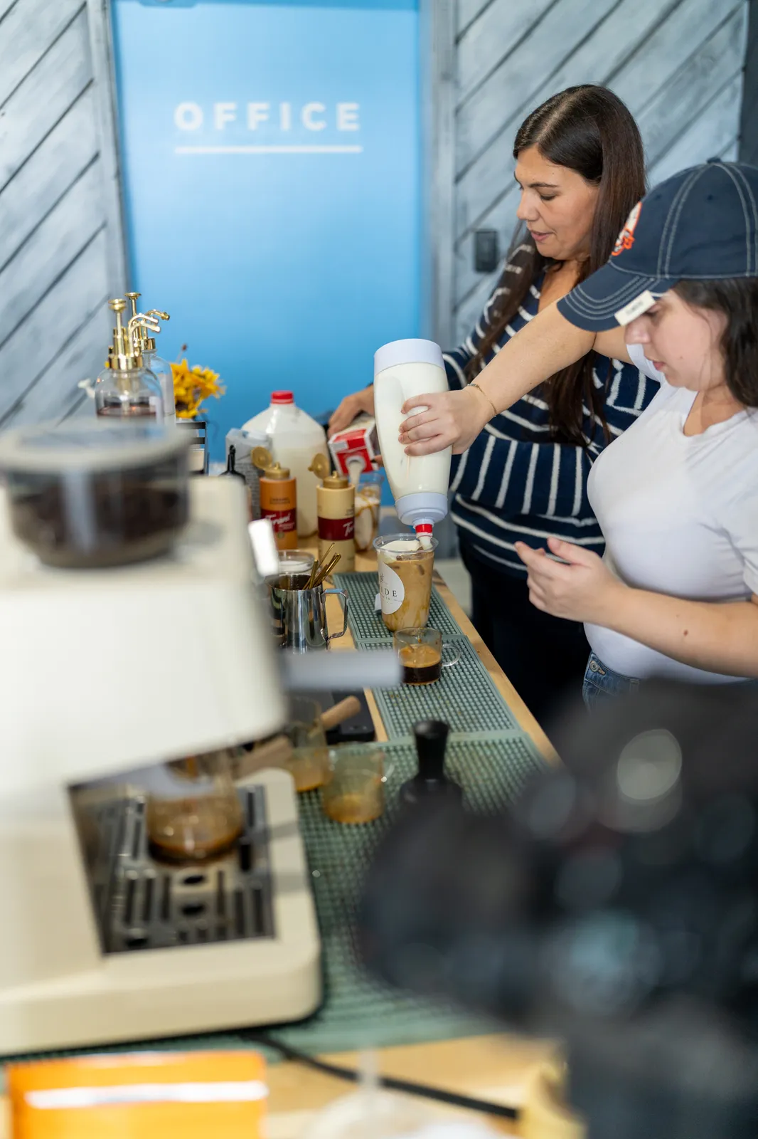 Two staff pour milk and prep drinks behind the espresso machine.