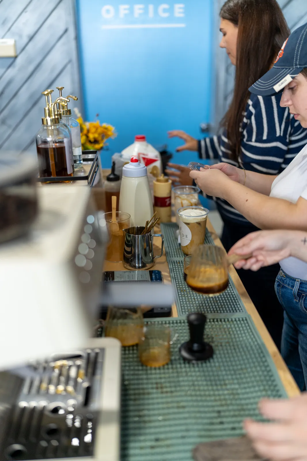 Syrups, a sunflower vase and espresso glasses line the bar as staff work through orders.