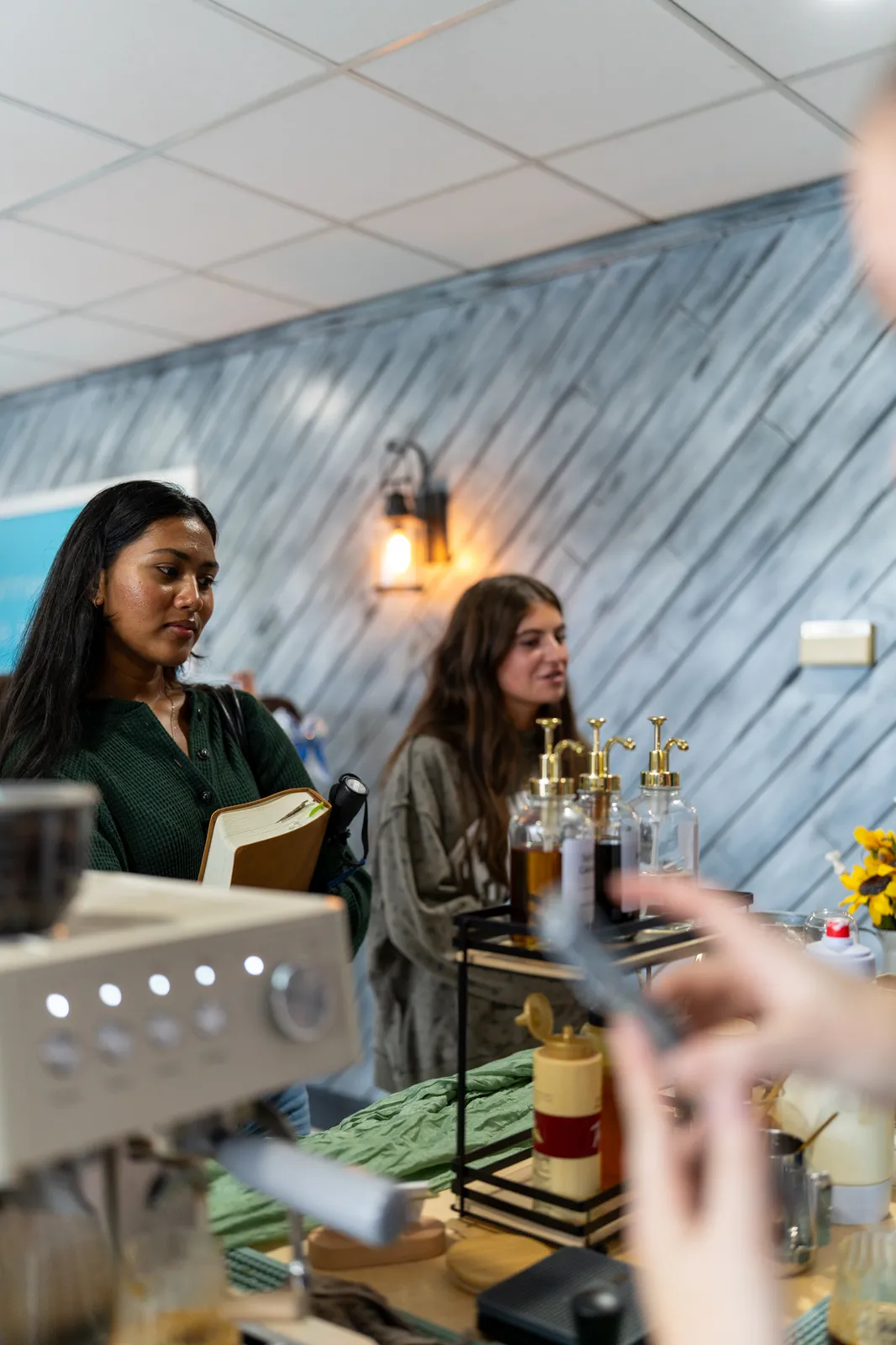 Two guests wait at the bar as the espresso machine runs in the foreground.