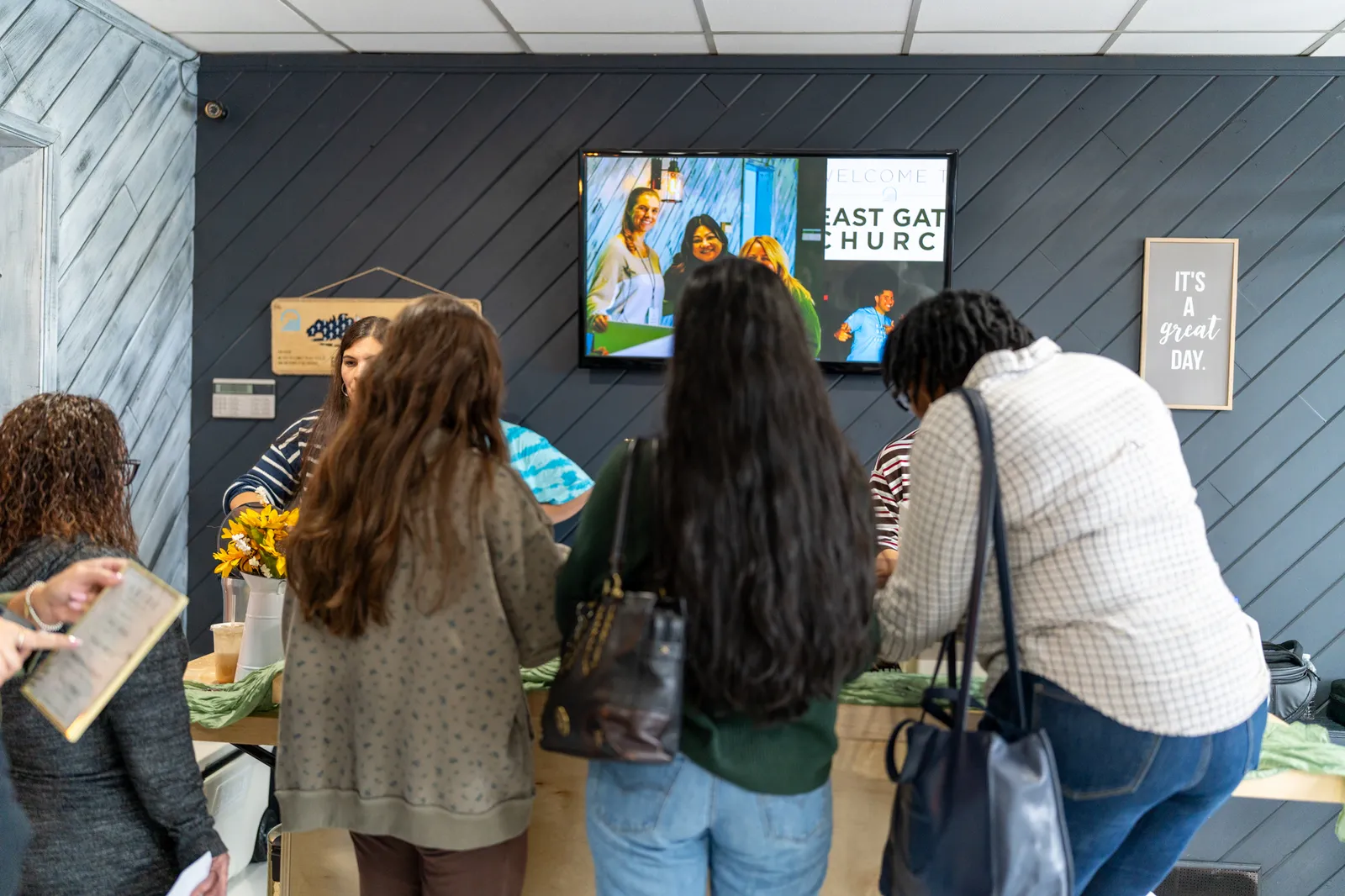 A group of guests crowds the counter to order beneath the lobby screen.