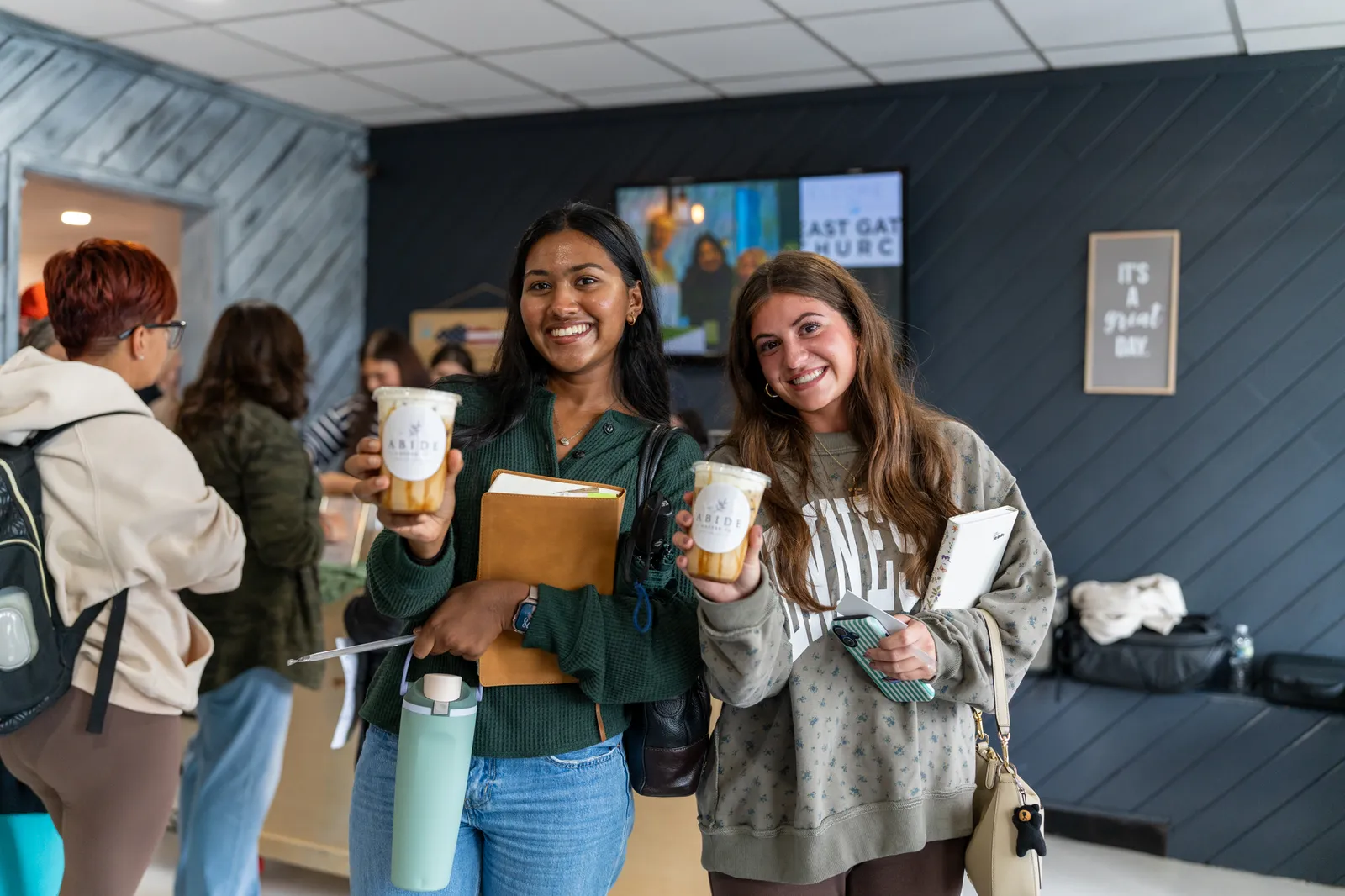 Two friends smile with their Abide iced drinks in hand.