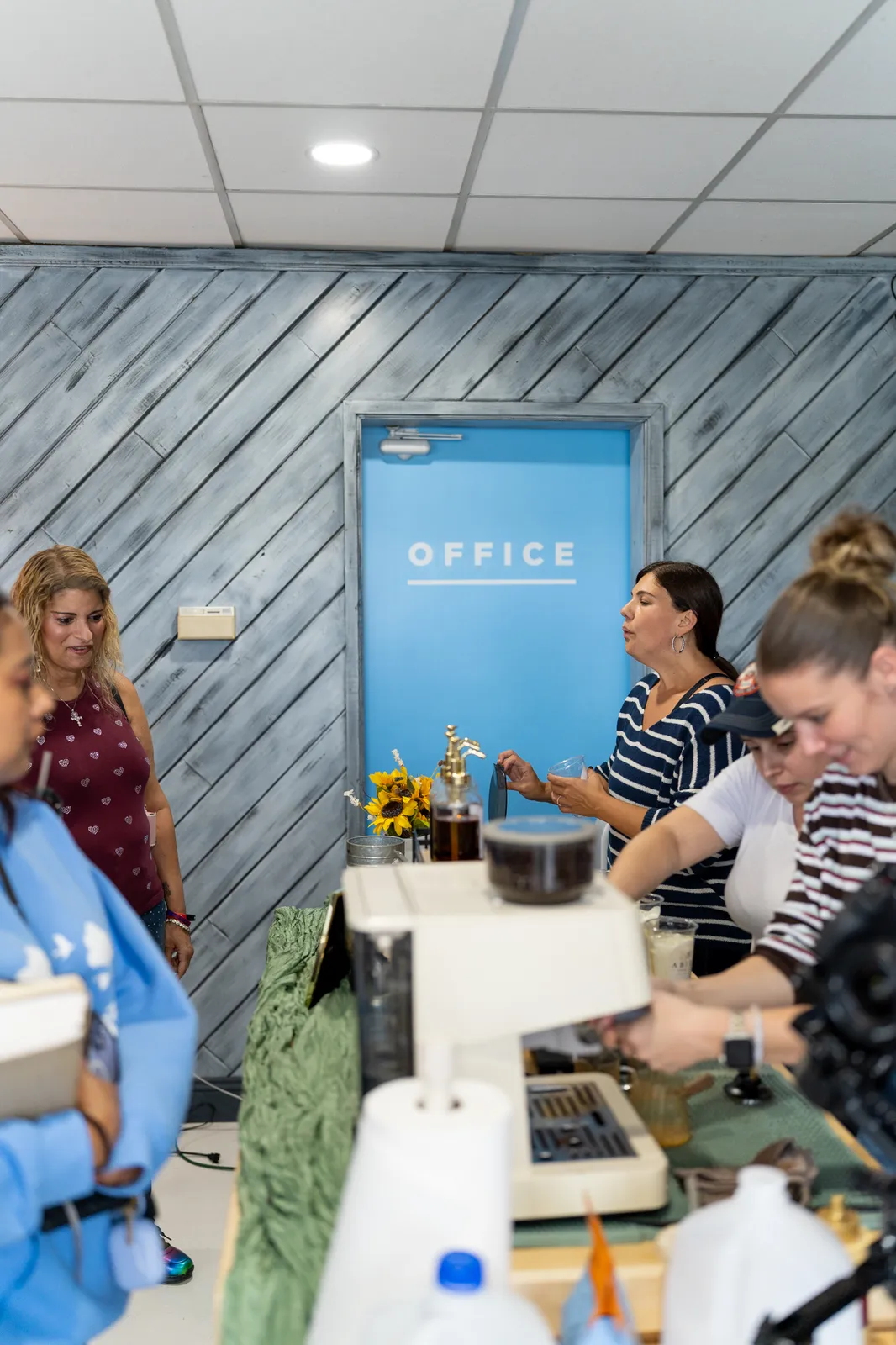 Baristas work a busy cart in front of the blue office door, sunflowers on the counter.