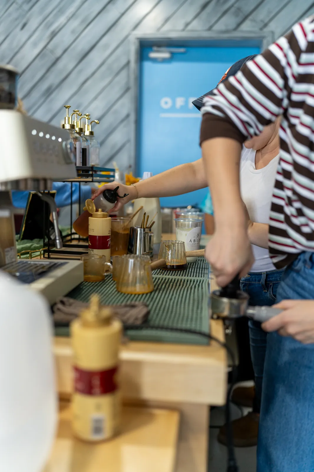 Hands reach across the bar as baristas tamp and pour at the espresso machine.