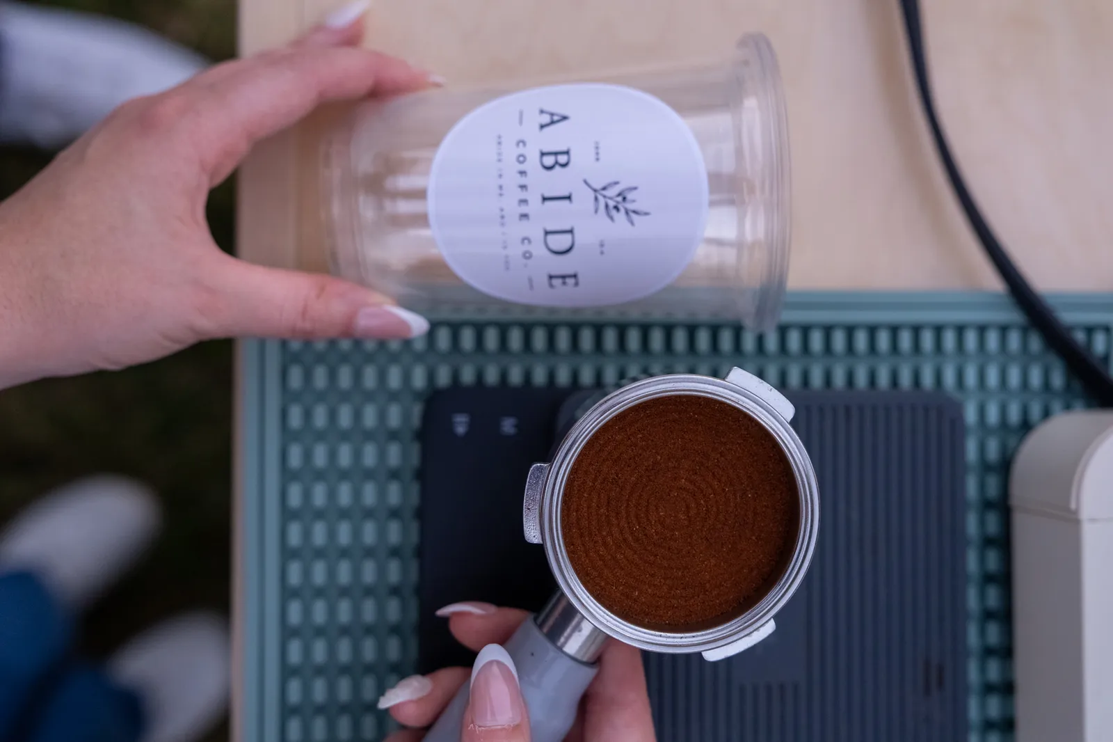 A branded Abide Coffee Co. cup and a freshly tamped portafilter rest on a sage-green bar mat.