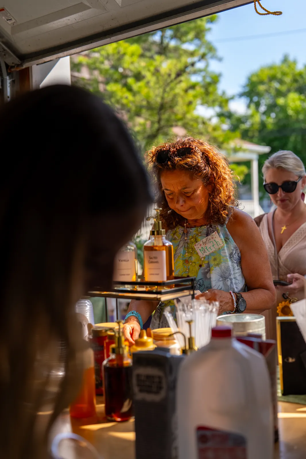 A barista finishes a drink at the cart as sunflowers glow in the foreground.